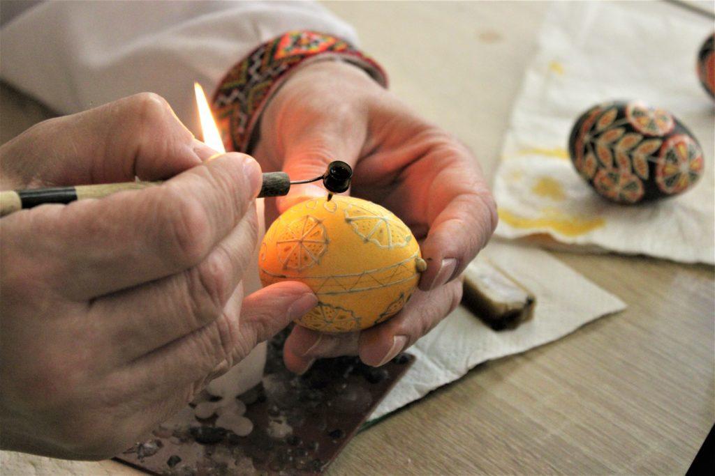 human hands decorate a yellow 'pysanka', or Ukrainian Easter egg, with candle wax into beautiful geometric designs