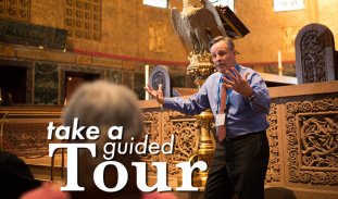 Take a guided Tour, featuring a tour guide enthusiastically talking to several people in the pews of Trinity Church Boston