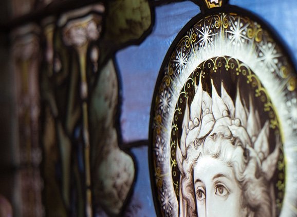 Stained glass window featuring a detail of Mary, Queen of Heaven, in black and white on a blue background.