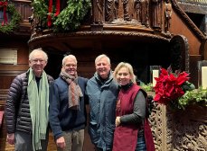 four adults smile in front of Trinity Church Boston's pulpit with noticeable greenery and poinsettias
