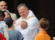 The Rev. Patrick Ward baptizes a baby while surrounded by smiling happy people