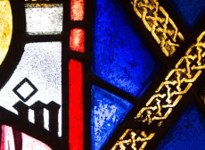 blue, red, white, and yellow stained glass detail in a geometric pattern, with the detail of a yellow 'X' over cobalt blue the prominent feature