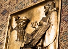 gold relief depicts a man in robes speaking, while another man in a scholar's hat writes in a book with a feather pen