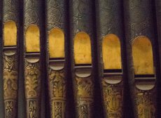 Decorated organ pipes cascading from upper left to lower right in tones of deep forest green and gold 