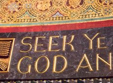 The text 'Seek Ye God' taken from Trinity Church Boston's chancel. The text is inlaid in gold over a polished green stone band, and above the stone is more gold leaf in a repeating circle pattern.
