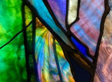 a detail from the 'Purity' stained glass window with green, purple, pink, blue, and swirling mixed glass in those colors