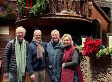 four adults smile in front of Trinity Church Boston's pulpit with noticeable greenery and poinsettias
